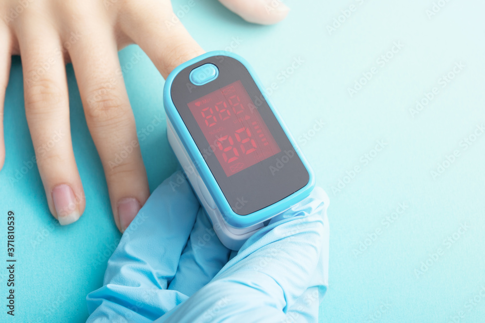 Monitoring of oxygen saturation of blood with a special device. Hand in a medical glove measures a patient on a blue background Monitoring of oxygen saturation of blood with a special device. Hand in a medical glove measures a patient on a blue background