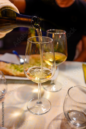 Pouring in glass  cold dry white wine in outdoor cafe at night in Italy