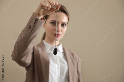 Psychotherapist with pendulum on beige background, space for text. Hypnotherapy session
