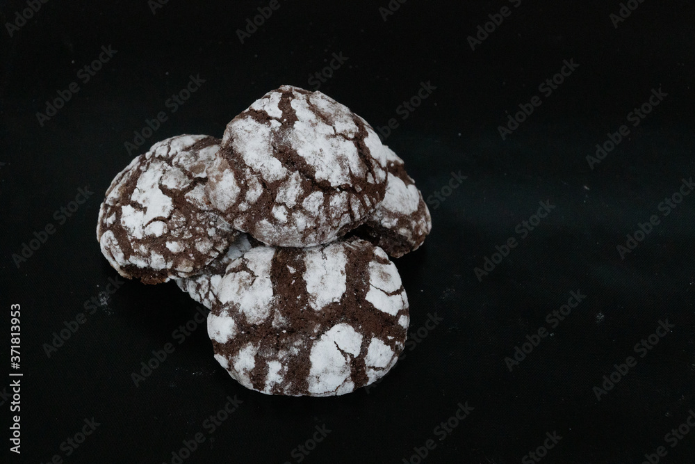 Homemade cookies with chocolate chips with powdered sugar on black background. Freshly baked choco cookie close up. Dark food. Cook at home.