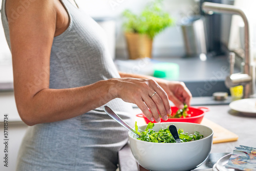 Eine schwangere Frau breitet in der Küche einen gesunden Salat zu