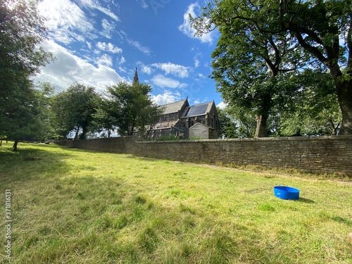 Grazing pasture, with a blue water bowl, trees, dry stone wall, and Denholme church, in the distance in, Denholme, Bradford, UK photo