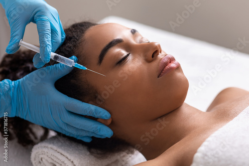Young black lady receiving eye zone injection at beauty salon