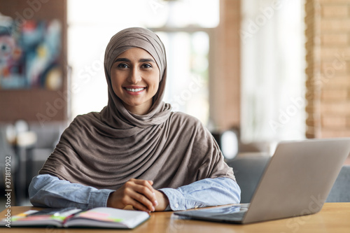 Smiling arab girl looking for job online, sitting at cafe