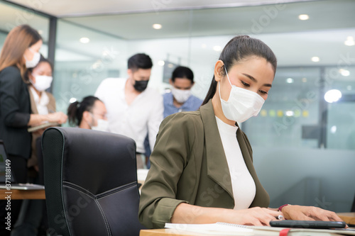 Portrait of Asian woman office worker wearing face mask working in new normal office and doing social distancing during corona virus covid-19 pandemic