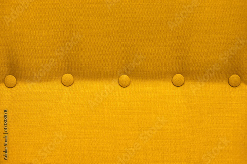 Texture of a close-up of a yellow fabric upholstery of an armchair with elements of accessories, background.