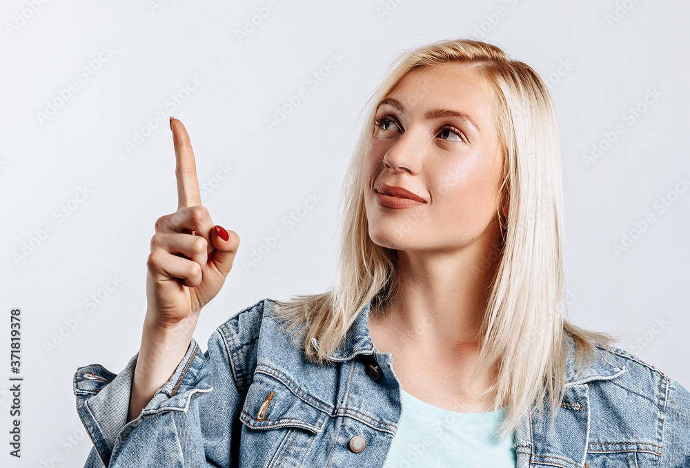 Portrait of a smiling girl pointing finger up at copyspace isolated on a white background. A woman points to an idea, a place for advertising. Positive blonde.