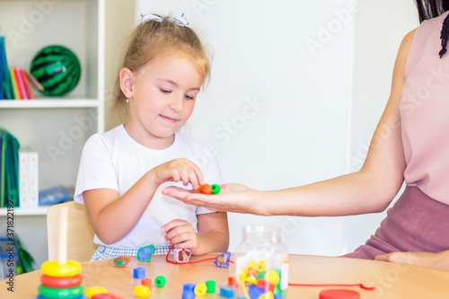 developmental and speech therapy classes with a child-girl. Speech therapy exercises and games with beads. The girl has beads in her hands