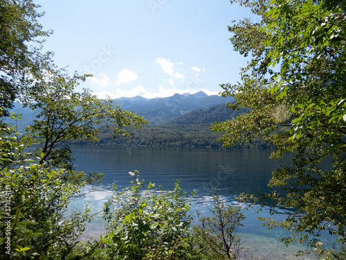 View of deep-blue lake with mountain range and blue sky in background and trees framing picture in foreground © Anita_S