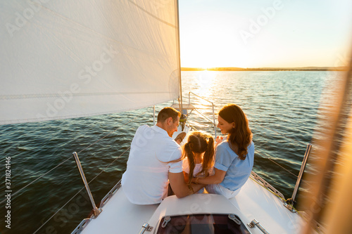 Family Yacht Sailing, Parents And Daughter Sitting On Deck, Back-View © Prostock-studio