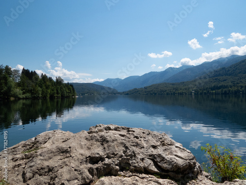 View towards reflecting lake with forest to the left and mountains to the right with rock surface in forefront implying viewer standing on stone