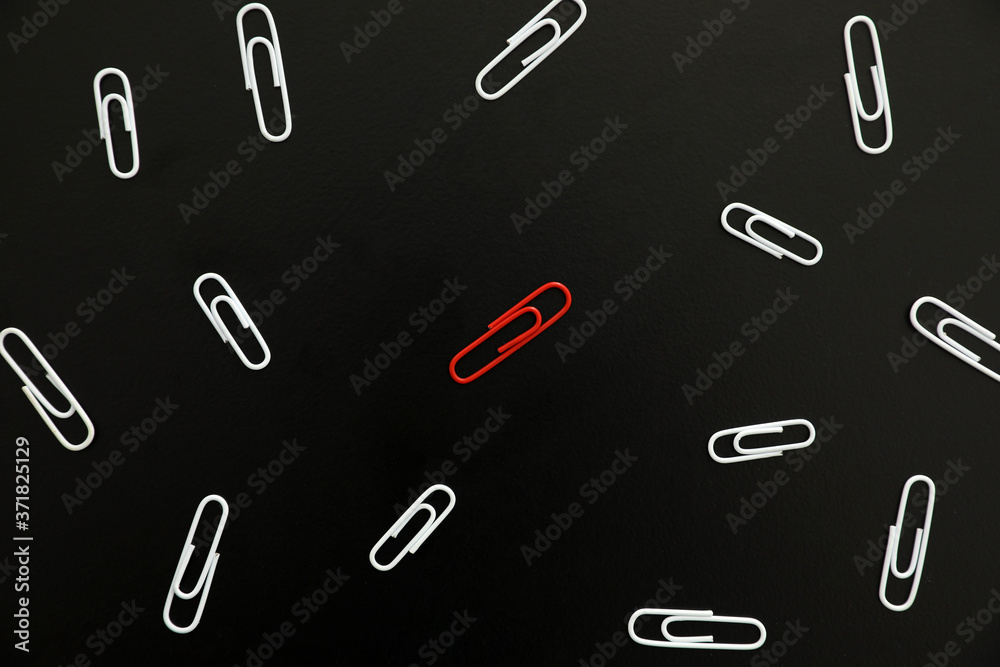 White paper clips and red one on black background, flat lay White paper clips and red one on black background, flat lay