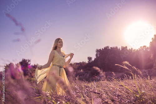 Blonde woman in a yellow dress in lavender field at sunset