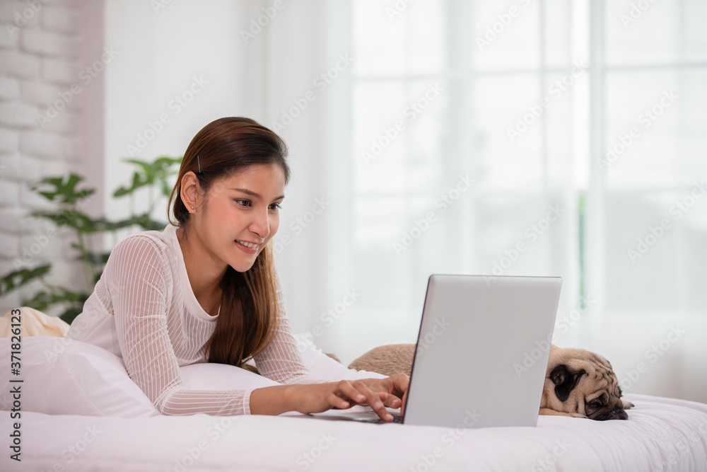 Woman typing and working on laptop with dog Pug breed lying on bed and looking on screen feeling happiness and comfortable at home,Friendly Dog at home Concept Woman typing and working on laptop with dog Pug breed lying on bed and looking on screen feeling happiness and comfortable at home,Friendly Dog at home Concept