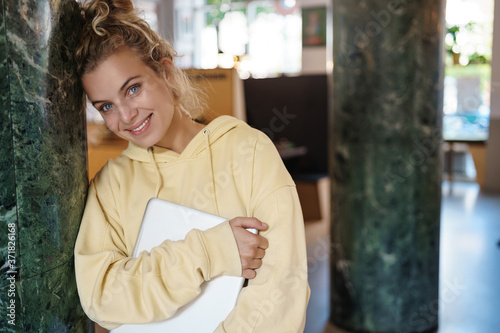 Smiling lovely woman standing in cafe and holding laptop. Female student studying online, remote from coffee shop. Freelancer working from favorite co-working space