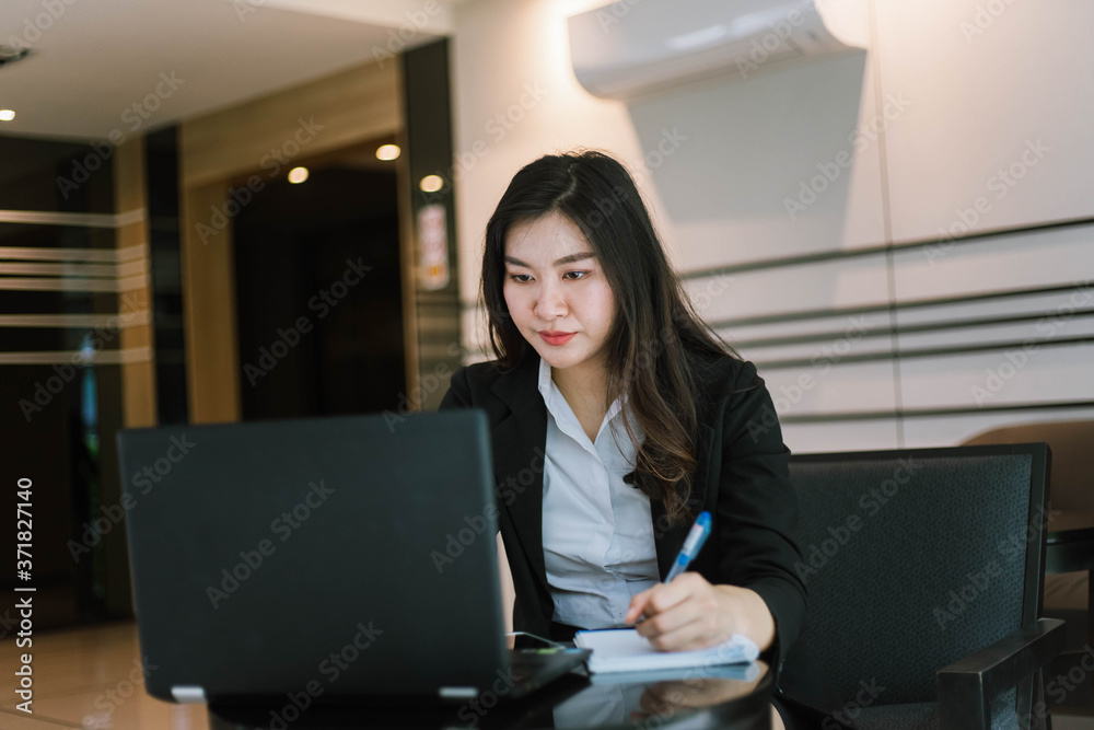 Beautiful young asian woman in suit using laptop and writing note Beautiful young asian woman in suit using laptop and writing note