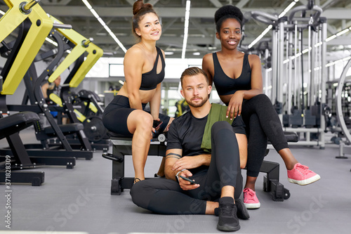 two fit girls training with personal trainer in gym  attractive african and caucasian women with strong male have rest after exercises