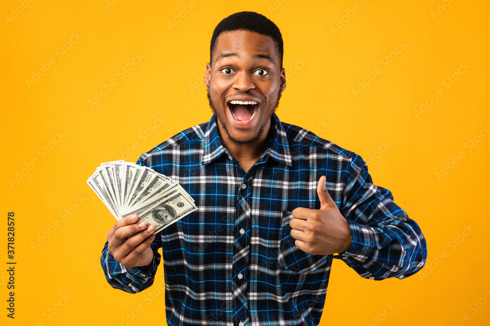 Excited African Guy Holding Money Gesturing Thumbs-Up Over Yellow Background Excited African Guy Holding Money Gesturing Thumbs-Up Over Yellow Background