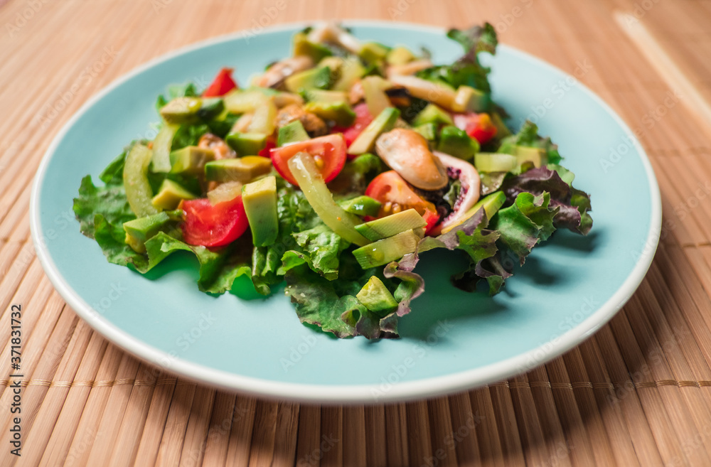 Salad with seafood with avocado, tomatoes, octopus and mussels in blue plate on wooden table. Concept of healthy diet food.