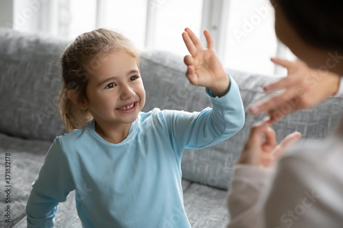 Adorable small preschool kid daughter showing okey sign, looking at deaf disabled mother indoors. Happy cute little child girl with hearing impairment enjoying communicating with physiotherapist. photo