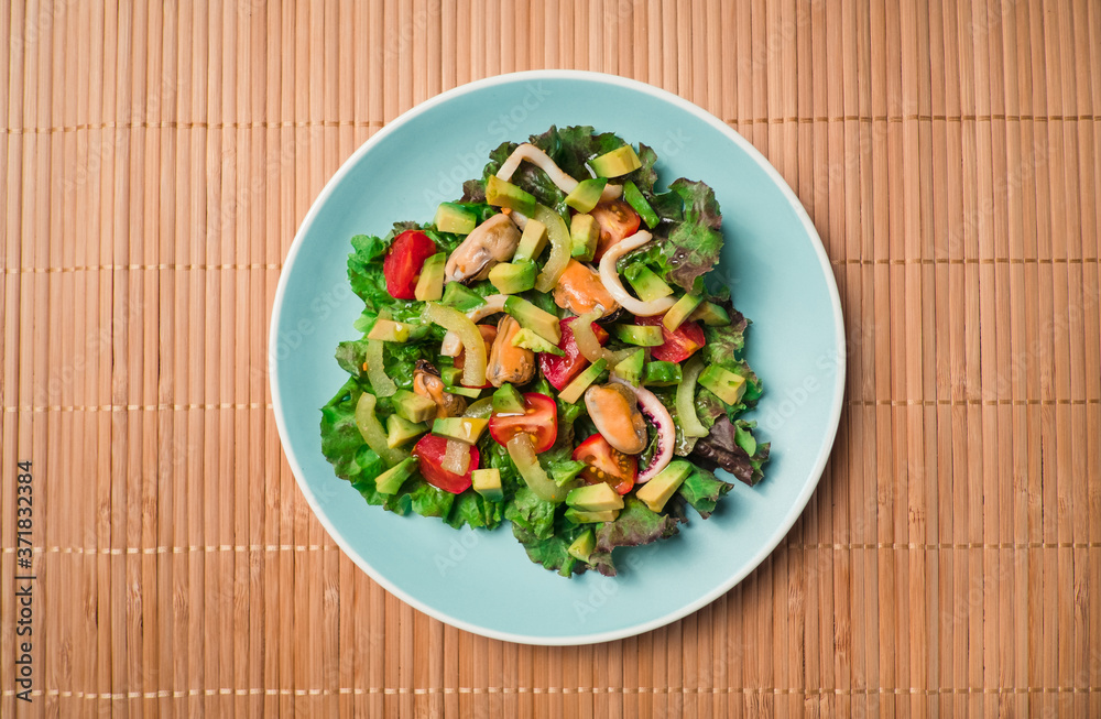 Flat lay - Asian Salad with seafood with avocado, tomatoes, octopus and mussels in blue plate on wooden table. Concept of healthy diet food. Flat lay - Asian Salad with seafood with avocado, tomatoes, octopus and mussels in blue plate on wooden table. Concept of healthy diet food.