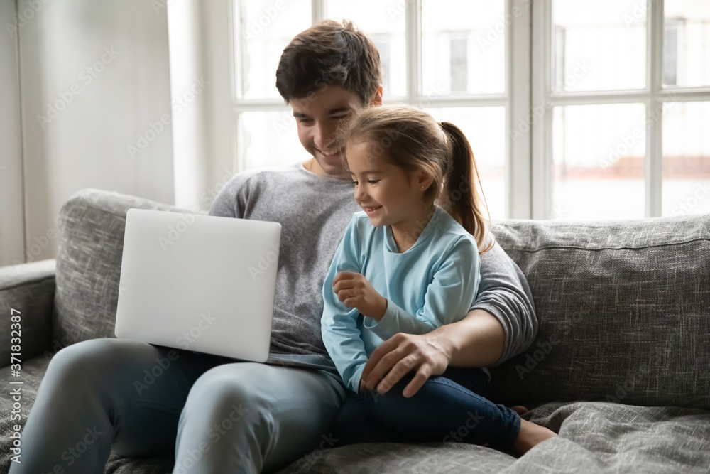 Adorable small preschool child girl enjoying learning using computer application with caring dad, sitting together on sofa. Happy father watching cartoons online on laptop with little daughter. Adorable small preschool child girl enjoying learning using computer application with caring dad, sitting together on sofa. Happy father watching cartoons online on laptop with little daughter.