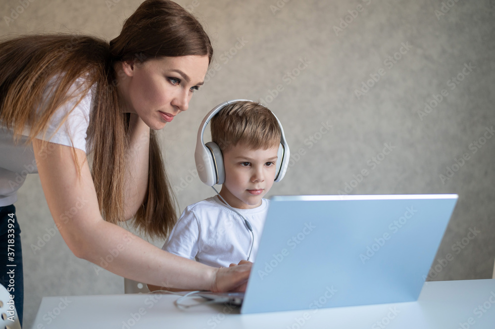 A caring mother helps her child do homework on a laptop. A woman and her little son are looking at a computer monitor. A caring mother helps her child do homework on a laptop. A woman and her little son are looking at a computer monitor.