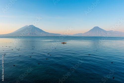 The volcanoes San Pedro, Toliman and Atitlan at sunrise by the Atitlan lake with a fisherman in a fishing boat between coots (Fulica atra), Panajachel, Guatemala.