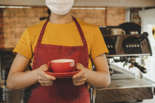 friendly waitress woman wearing protection face mask waiting for serving hot coffee red cup to customer in cafe coffee shop, cafe restaurant, service mind, new normal, food and drink delivery concept