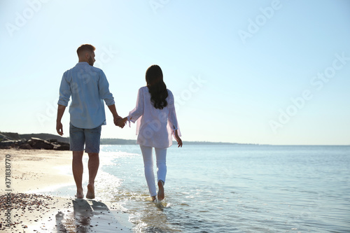 Young couple walking on beach near sea, back view. Honeymoon trip