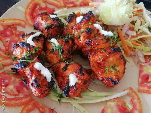 Fototapeta Naklejka Na Ścianę i Meble -  Close-up view of an Indian dish chicken Tikka tandoori, laid out on rings of tomatoes and garnished with salad