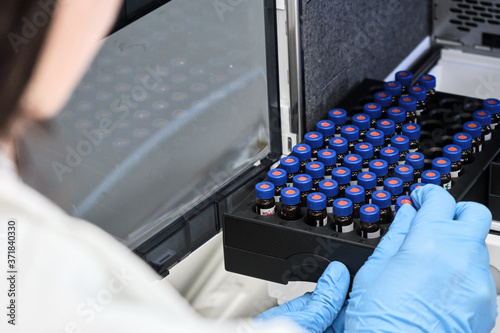 Scientist in a white lab coat putting vial with a sample into autosampler of HPLC system. High performance liquid chromatography at chemical laboratory. Developing of pharmaceuticals or vaccine photo