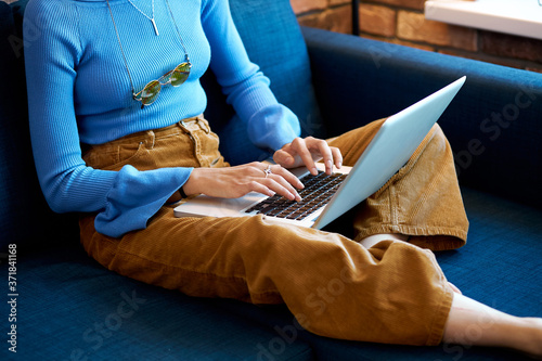 cropped woman using laptop at home, she sit on sofa in living room, wearing casual clothes. typing on the keyboard