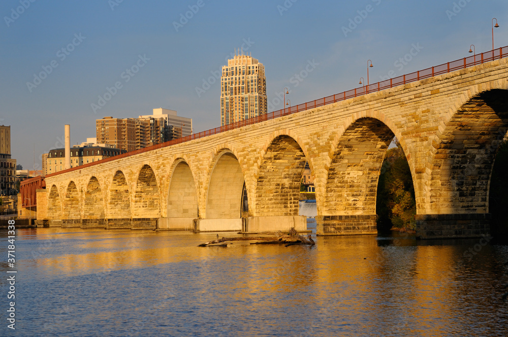 The Stone Arch Bridge reflected in the golden glow of sunrise on the Mississippi river at Minneapolis