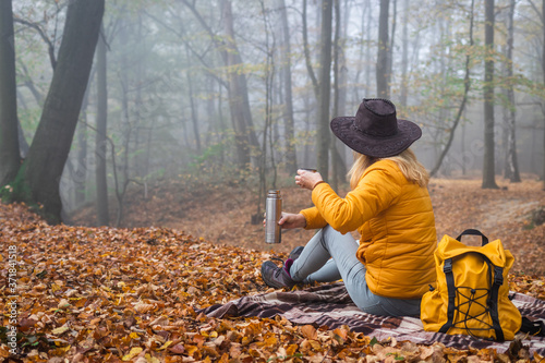 Hiker sitting on picnic blanket and drinking hot drink in autumn forest. Woman resting in nature during hike © encierro