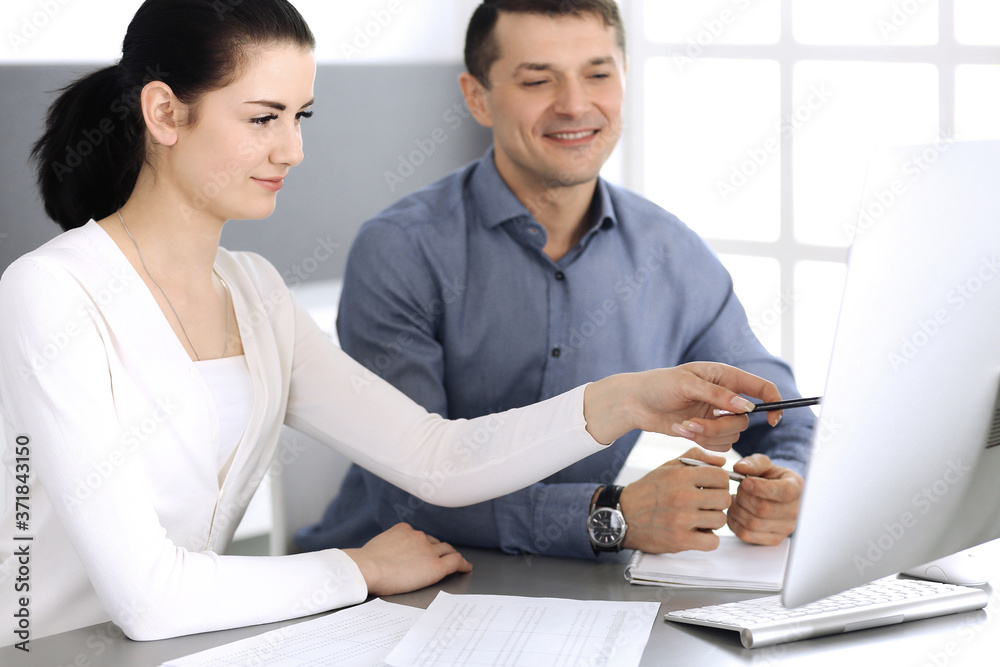 Cheerful smiling businessman and woman working with computer in modern office. Headshot at meeting or workplace. Teamwork, partnership and business concept Cheerful smiling businessman and woman working with computer in modern office. Headshot at meeting or workplace. Teamwork, partnership and business concept
