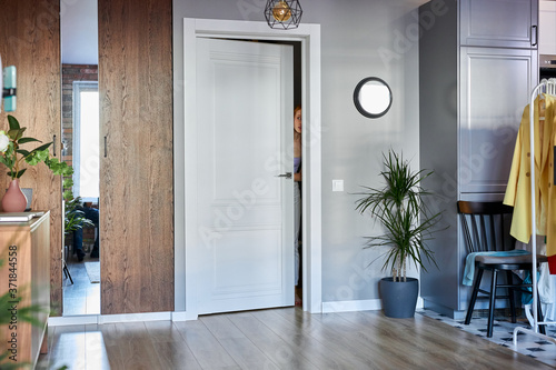 unrecognizable woman peeping out of the door in new apartment, young female going to live in this room alone