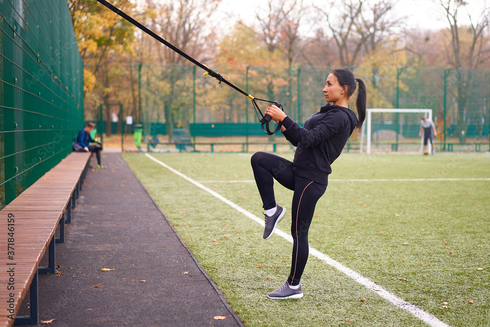 Girl athlete training using trx on sportground. Mixed race young adult woman do workout with suspension system. Healthy lifestyle. Stretching outdoors playground.