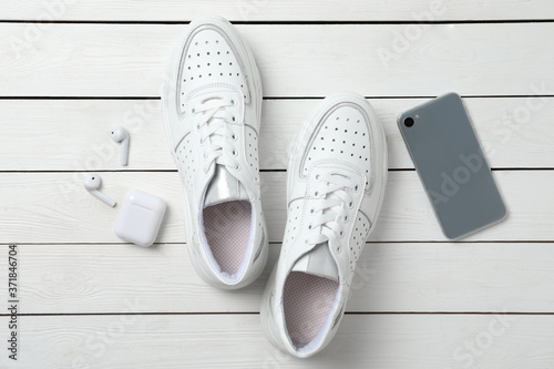 Pair of stylish shoes, modern smartphone and wireless earphones on white wooden table, flat lay