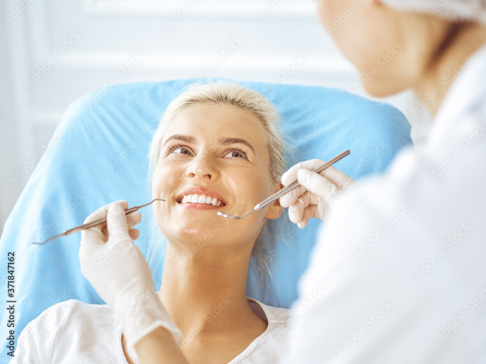 Smiling blonde woman examined by dentist at dental clinic. Healthy teeth and medicine concept Smiling blonde woman examined by dentist at dental clinic. Healthy teeth and medicine concept