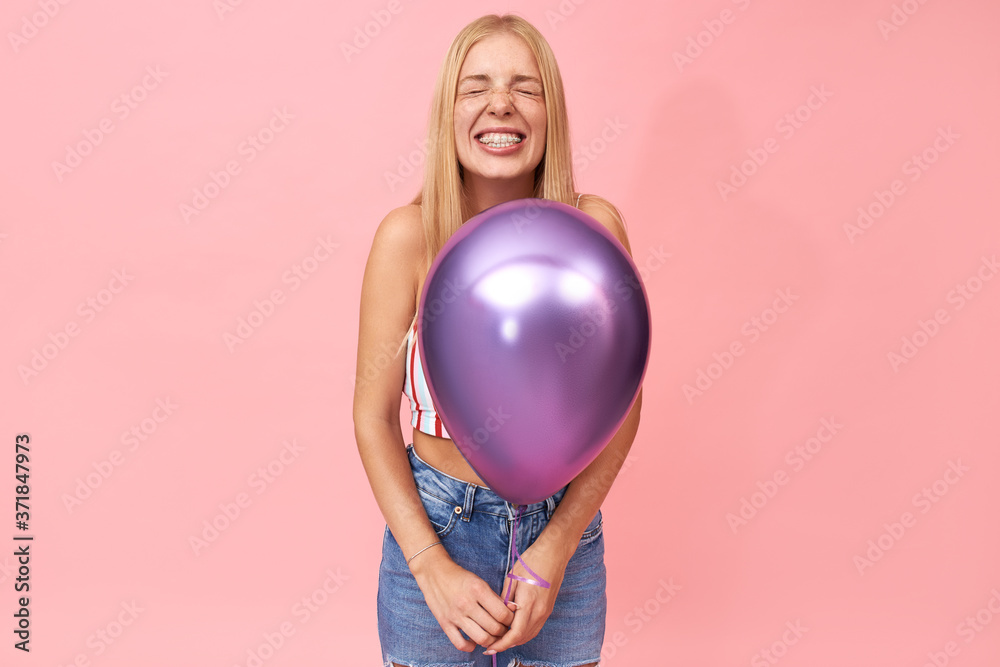 Positive emotions, joy, special occasions, celebration and holidays concept. Portrait of stylish adorable teen girl with braces closing eyes and smiling broadly, posing isolated with helium balloon Positive emotions, joy, special occasions, celebration and holidays concept. Portrait of stylish adorable teen girl with braces closing eyes and smiling broadly, posing isolated with helium balloon