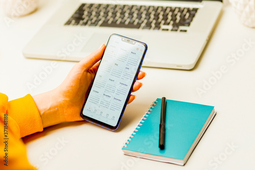 Woman holding phone and using calendar to make her plan in the notepad photo