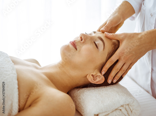 Beautiful brunette woman enjoying facial massage with closed eyes. Relaxing treatment in medicine and spa center concepts