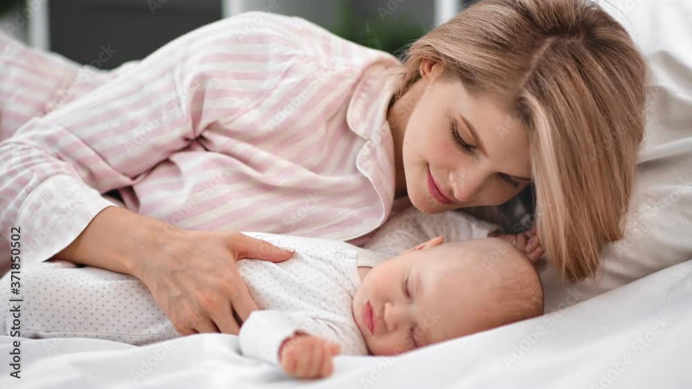 Pleasant mother admiring sleeping baby lying on bed together. Shot on RED Raven 4k Cinema Camera Pleasant mother admiring sleeping baby lying on bed together. Shot on RED Raven 4k Cinema Camera