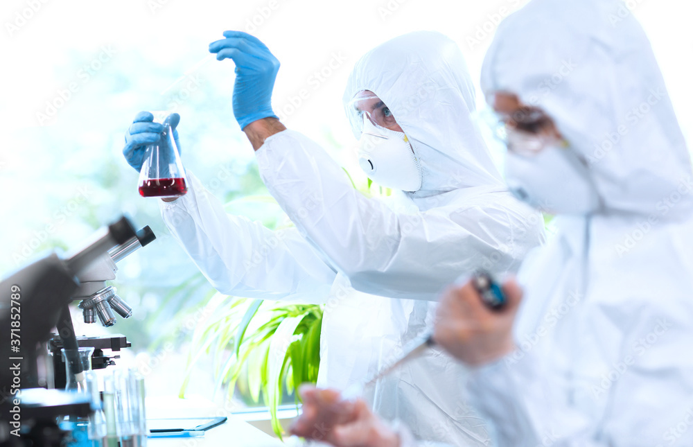 Fototapeta premium Scientists in protection suits and masks working in research lab using laboratory equipment: microscopes, test tubes.