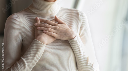 Close up focus on female hands, folded on chest. Happy young woman employee feeling thankful indoors, praying for good luck on important business meeting, dreaming of future, appreciation concept. photo
