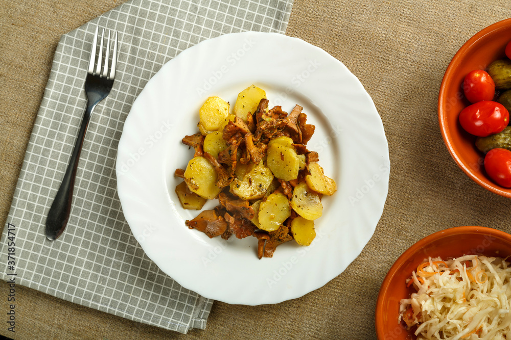 a plate of potatoes with larvae mushrooms on a napkin and a fork next to pickled cucumbers and tomatoes and cabbage. a plate of potatoes with larvae mushrooms on a napkin and a fork next to pickled cucumbers and tomatoes and cabbage.