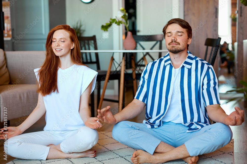 beautiful caucasian couple practice yoga at home, they sit in lotus pose, meditate, wearing domestic wear beautiful caucasian couple practice yoga at home, they sit in lotus pose, meditate, wearing domestic wear