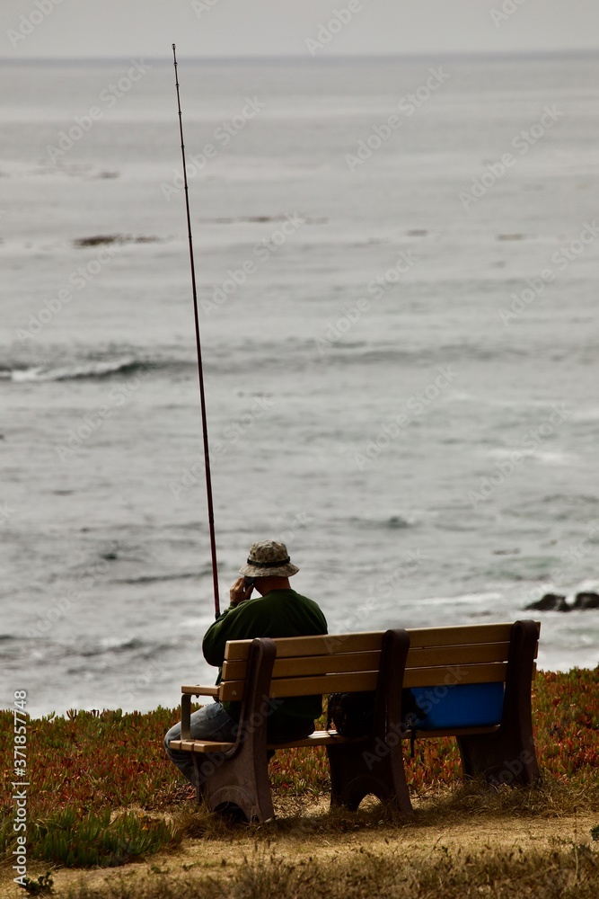 a solitary fisherman using his phone looks out to sea