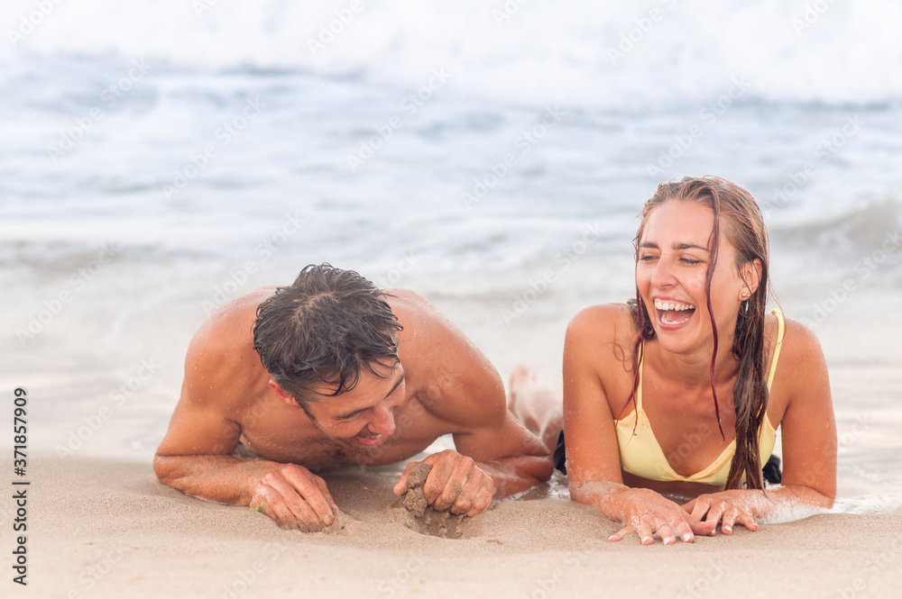Summer sea vacation concept. Portrait of young smiling and laughing couple, laying near the water